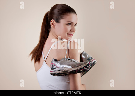 Une jeune femme tenant une paire de chaussures de formation par-dessus son épaule Banque D'Images