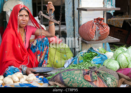 Les femmes vêtus de rouge vente sari pesant légumes avec solde au marché en Bundi, Rajasthan, Inde Banque D'Images