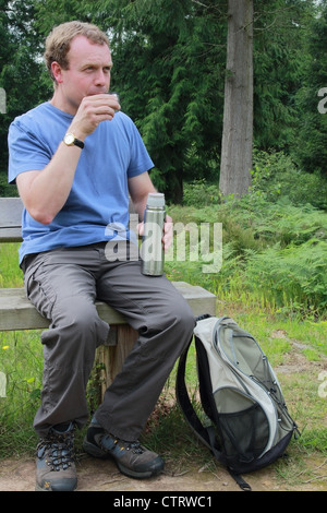 Homme de race blanche Walker boire d'une Thermos whist assis sur un banc en bois en été, MODÈLE BRITANNIQUE PUBLIÉ Banque D'Images