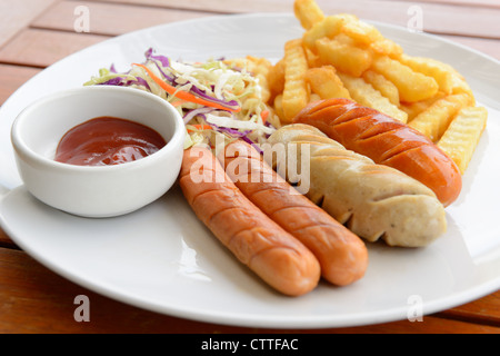 Saucisse mixte servi avec pommes de terre frites dans l'assiette blanche mis sur la table en bois Banque D'Images