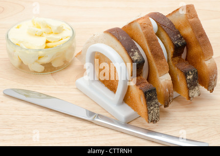 Tranches de pain grillé dans un rack blanc chine toast avec du beurre et un couteau de table. Banque D'Images