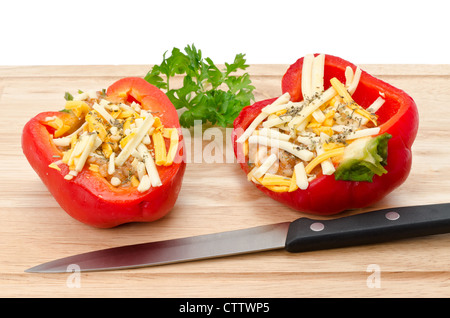 Deux poivrons farcis rouge fraîchement préparé avec du fromage râpé et le riz brun sur une planche à découper en bois Banque D'Images