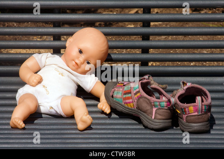 Une poupée en plastique qui est assis à côté de chaussures de bébé sur un banc métallique à Georgetown Waterfront Park, Washington, DC Banque D'Images