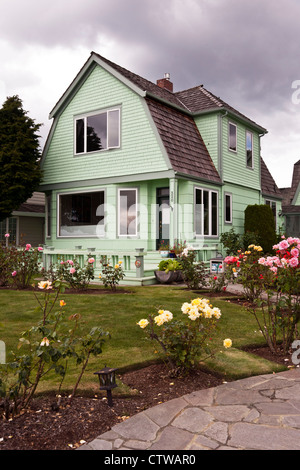 Vieille maison en bois peint vert pâle avec toit en mansarde et belle pelouse avec jardin de roses sur le front de mer d'Edmonds Washington Banque D'Images