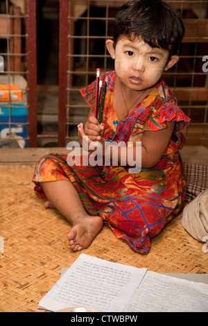 Le Myanmar, Birmanie. Petite fille birmane, crayons, Bloc-notes et de l'écriture. Elle a thanaka coller sur son visage, un cosmétique crème solaire. Banque D'Images