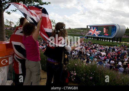 Les familles et les spectateurs chantent l'hymne national britannique au cours d'une cérémonie de remise des médailles d'or olympique de tir Peter Robinson dans le Parc olympique au cours de l'Jeux olympiques de 2012 à Londres. La plantation de 4 000 arbres, 300 000 plantes de milieux humides et plus de 150 000 plantes vivaces plus riches en nectar de fleurs sauvages faire un cadre coloré pour les Jeux. Ce terrain a été transformé pour devenir un 2,5 Km2 complexe sportif, une fois que les entreprises industrielles et maintenant le lieu de huit salles dont l'arène principale, centre aquatique et le vélodrome et le Village Olympique des athlètes. Banque D'Images