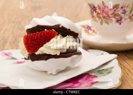 Gâteau meringue fraîche d'une épaisse couche de crème fouettée et d'une fraise servi avec une tasse de thé dans une tasse et soucoupe en porcelaine Banque D'Images