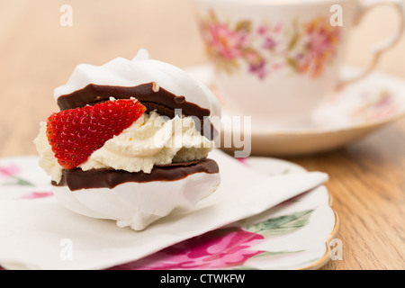 Gâteau meringue fraîche d'une épaisse couche de crème fouettée et d'une fraise servi avec une tasse de thé dans une tasse et soucoupe en porcelaine. Banque D'Images