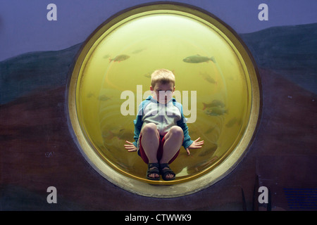 Jeune garçon assis dans la fenêtre d'un aquarium, Natur- und Umweltpark Guestrow, Schleswig-Holstein, Allemagne Banque D'Images