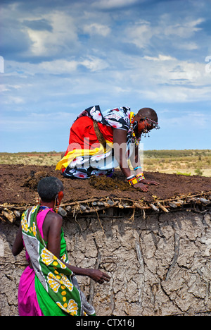Femme Masai l'application d'un mélange de fumier de bovins et de boue à un le toit d'une maison dans un village de la Masai Mara, Kenya, Afrique Banque D'Images