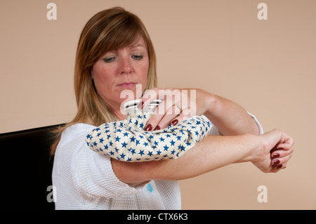 Femme tenant une poche de glace sur un coude blessé Banque D'Images