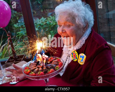 Gâteau d'anniversaire pour les personnes âgées, une dame qui se moque de sourire en célébrant son anniversaire de 97th ans à la maison de famille avec un gâteau mousseux avec 9-7 badges d'anniversaire et ballons Banque D'Images
