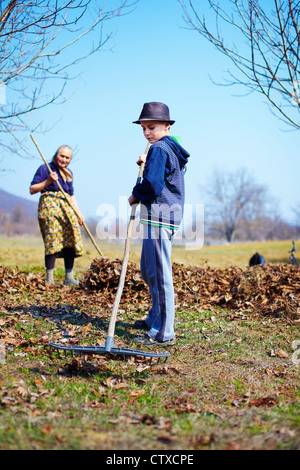 Grand-mère et petit-fils du grand ménage de printemps le verger de noyers avec râteaux Banque D'Images