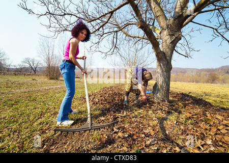 Hauts femme rurale et sa fille avec des râteaux, le nettoyage de printemps dans un verger de noyers Banque D'Images