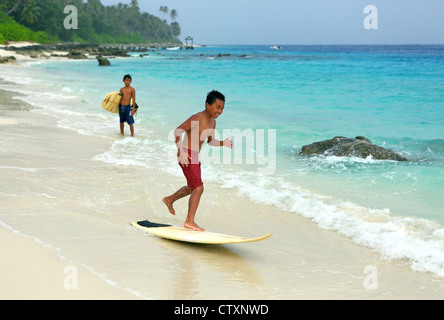 Les garçons s'amuser conseil écrémé surf sur la plage à l'île dans l'Hinako îles au large de la côte de l'Océan indien du nord de Sumatra. Banque D'Images