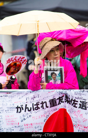 Les partisans d'athlétisme japonais attendre sous la pluie pour le Marathon, Jeux olympiques, Londres, 2012. Banque D'Images