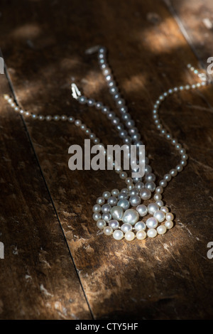 Collier de perles sur un plancher en chêne dans la lumière du soleil Banque D'Images