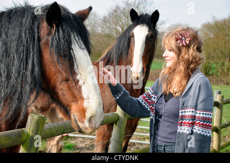 Près d'un joli tir, Long haired, adolescente de caresser un cheval avec un autre cheval à la recherche sur. Banque D'Images