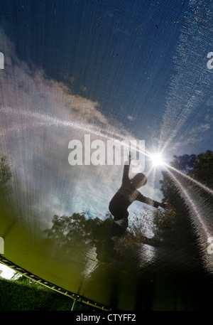 Grand angle shot contre le soleil d'une petite fille sur un trampoline, vue du dessous Banque D'Images