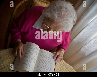 Vieille dame lecture livre à table dans la fenêtre de lumière naturelle Banque D'Images