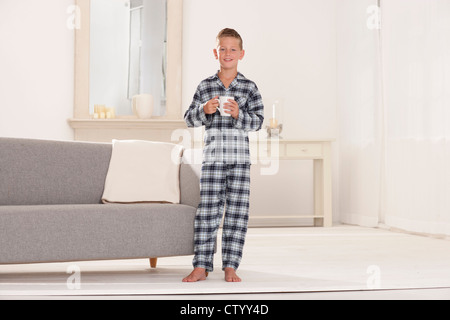 Garçon en pyjama avec mug in living room Banque D'Images