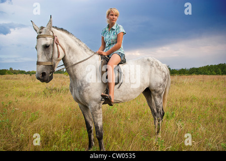 Les jeunes femmes adultes ride sur cheval gris sur un pré, est de l'Europe Banque D'Images