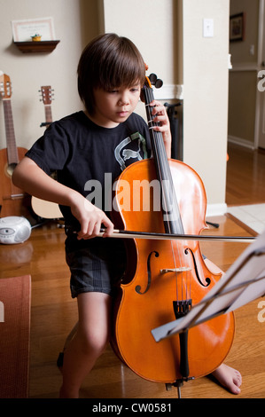 Garçon de 8 ans Japonais-américain pratiques leçons de musique jouer du violoncelle et la lecture de partitions à la maison Banque D'Images