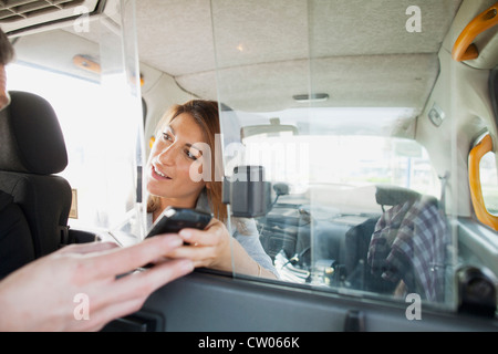 Woman handing téléphone cellulaire pour chauffeur de taxi Banque D'Images