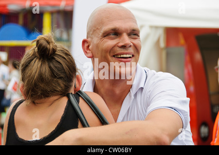 Baldheaded happy smiling Caucasian young adult man étreignant un jeunes femmes adultes avec ses cheveux en chignon bun Banque D'Images