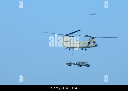 Un hélicoptère Apache AH-64D assure la sécurité d'un CH-47 Chinook transportant un HMMWV et un Howitzer lors d'une démonstration de chargement de harnais à l'aérodrome de l'armée Campbell mardi. Cette démonstration a été une répétition de l'assaut aérien qui aura lieu samedi dans le cadre du spectacle aérien de fort Campbell, qui commence à 10 heures Banque D'Images