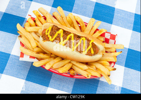 Un chilidog avec de la moutarde dans un panier de frites fraîches sur une nappe à carreaux bleu et blanc. Banque D'Images