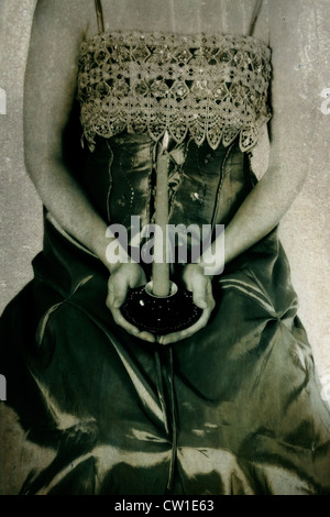 Une femme dans une période dress holding un cierge allumé sur ses genoux