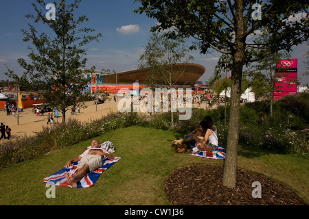 Brit spectateurs profitez d'un été chaud sur leur Union jack , dans le Parc olympique au cours de l'Jeux olympiques de 2012 à Londres, assis sur l'herbe verte situé sur une colline en face de l'emblématique site vélodrome. Le Parc olympique de Londres, à moins d'un kilomètre carré, est le plus grand nouveau parc dans la ville depuis plus de 100 ans. La plantation de 4 000 arbres, 300 000 plantes de milieux humides et plus de 150 000 plantes vivaces plus riches en nectar de fleurs sauvages faire un cadre coloré pour les Jeux. (Plus le sous-titrage dans Description..) Banque D'Images