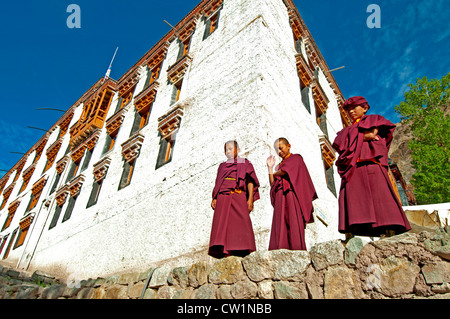 Trois jeunes moines en robe robes rouge debout sur un mur de pierre en face d'un immeuble au monastère de Hemis Ladakh, Inde Banque D'Images