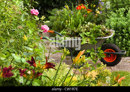 Le nettoyage de l'été jardin plein de fleurs et de brouette avec jardin-déchets, les plantes et les mauvaises herbes - horizontal Banque D'Images