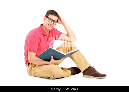 Jeune homme assis sur le plancher et la lecture d'un livre, isolé sur fond blanc Banque D'Images