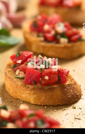 Des antipasti italiens Bruschetta croustillant appelé surmontée de tomate, ail et basilic sur planche de bois Banque D'Images