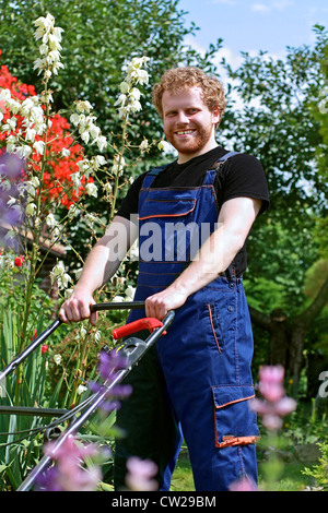 Un jeune jardinier heureux, couper le gazon entre les belles fleurs dans le jardin Banque D'Images