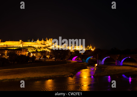 Remparts de l'antique lumineux de Carcassonne avec arches du pont bleu rose lumineux en noir ciel de nuit. Banque D'Images