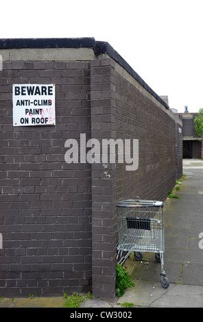 Un chariot de supermarché abandonné et un mur avec un signe d'avertissement montée anti-peinture. Banque D'Images