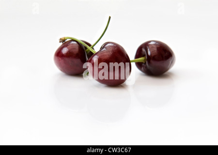 Close up de trois cerises rouges mûrs sur fond réfléchissant blanc Banque D'Images