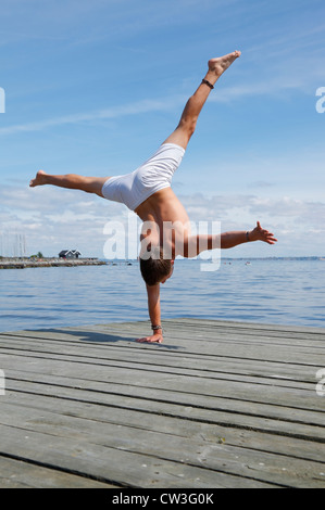 Un adolescent à un seul bras acrobatique headphones une jetée à la plage un chaud après-midi d'été. Le Danemark. Banque D'Images