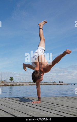 Un adolescent à un seul bras acrobatique headphones une jetée à la plage un chaud après-midi d'été. Le Danemark. Banque D'Images