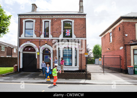 Les familles et les enfants attendent le passage de la flamme olympique, tout en agitant des drapeaux de l'Union à l'extérieur de leur maison décorée Banque D'Images