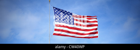Voici une photo d'un drapeau américain sur un mât, ondulant dans le vent contre un ciel bleu. Banque D'Images