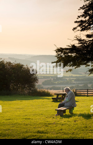 Vieux monsieur assis sur un banc de parc de pays bénéficiant du soleil du soir Banque D'Images