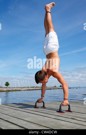 Faire un adolescent mâle headphones push-up poignées sur une jetée à la plage un chaud après-midi d'été. Banque D'Images