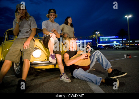 Des amis à l'aide de téléphones mobiles et de jouer de la guitare par une voiture à l'aire de stationnement Banque D'Images
