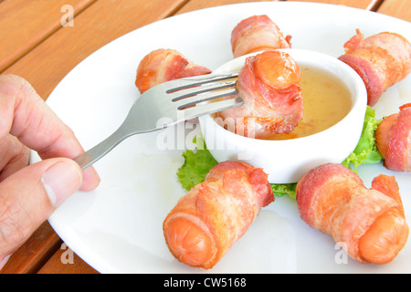 Le mâle part utiliser fork choisissez des saucisses au lard en enrobé de sauce. Banque D'Images