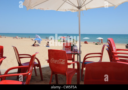 Des chaises en plastique rouge empilés et placés à côté de la table, beach bar, restaurant, bain de sable, parasols, journée ensoleillée, Punta Umbria. Banque D'Images